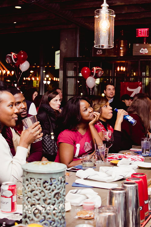 People enjoying a University of Alabama football game during happy hour with beer, cocktails, and food
