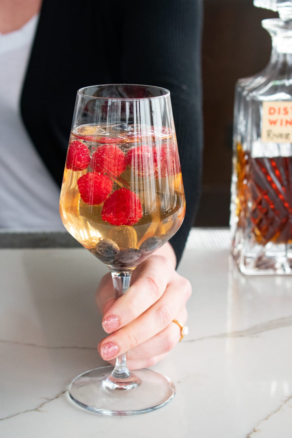 Woman holding sparkling wine topped with fresh fruit at District Winery