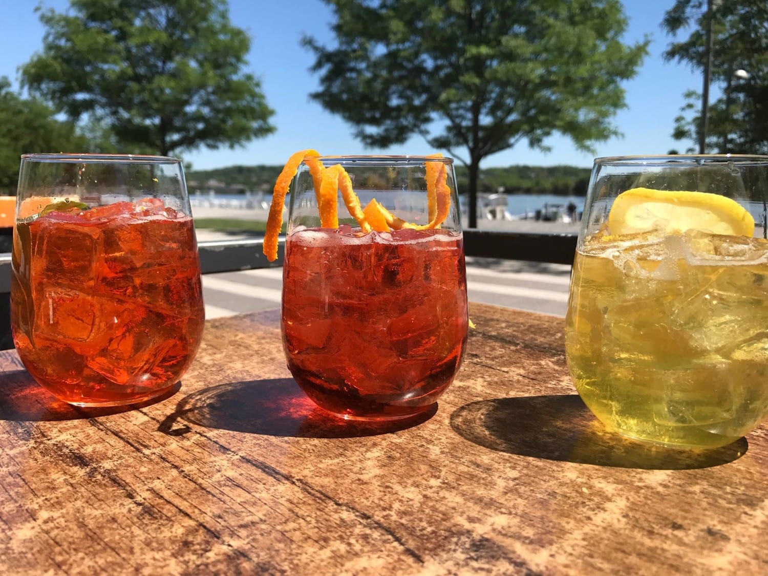 Three cocktail glasses garnished with fruit on open air table by the water