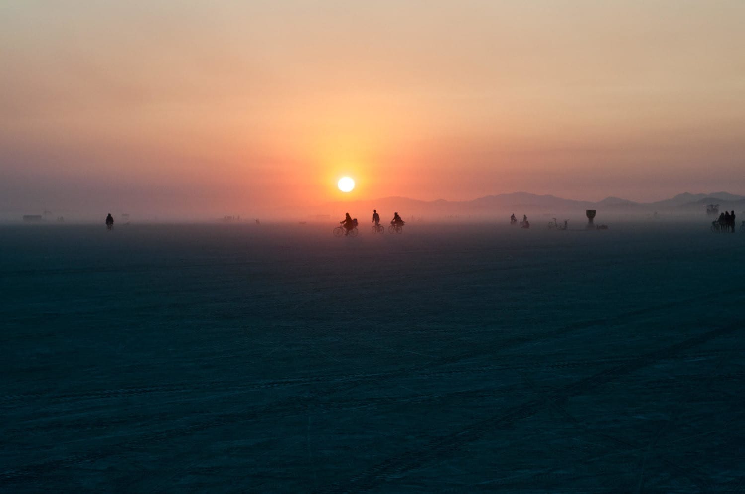 A sunset in the mountainous landscape of the Black Rock Desert, Nevada behind several bike riders.